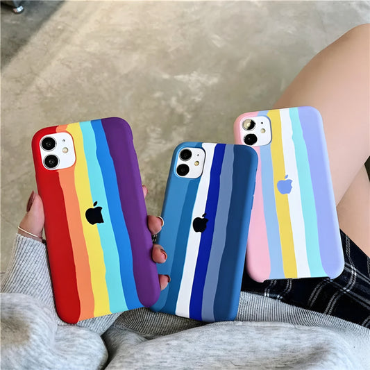 A person holds three iPhones, each adorned with ZIVIKART Silicone Cases for iPhone 12 Series featuring colorful vertical, wavy stripes. One showcases rainbow colors, another in various blues, and a third in pastel tones. These wireless charging compatible cases also proudly display the Apple logo in black or white.